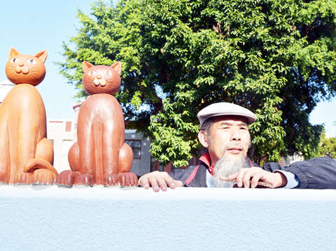 县籍艺术家吴鼎信以巧手童心塑造猫塑像，塑立在墙头的猫咪群像成为路旁的可爱风景。（詹宗翰摄）