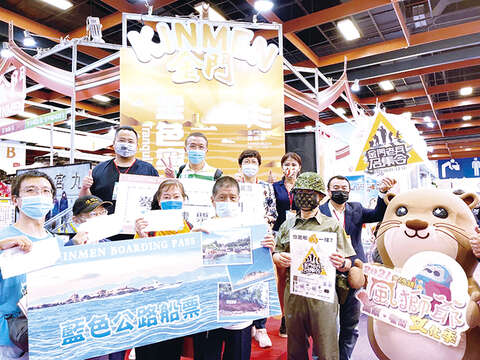 台北國際旅展金門館現場加碼送來回機票及藍色公路船票（第二排左起金門縣政府觀光處長丁健剛、獲得機票的林先生、台灣旅遊交流協會理事長賴瑟珍）。（觀光處提供）